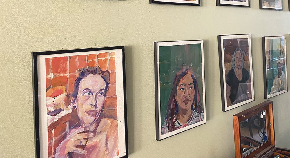 Multiple paintings hanging on a matcha green wall, handmade by one of our artist panelist