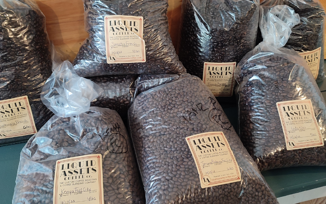 Multiple plastic bags of dark roast coffee beans are laying on a wooden bench,