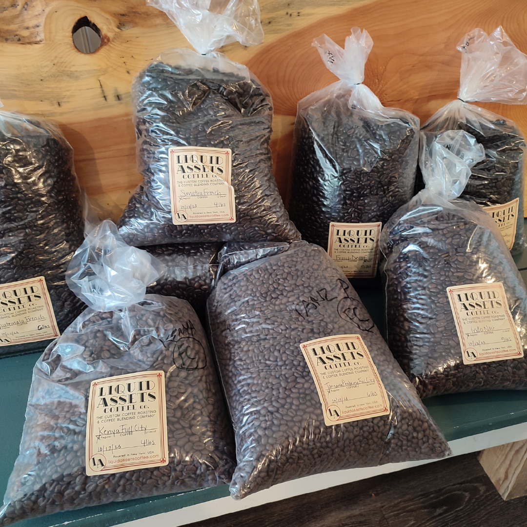Multiple plastic bags of dark roast coffee beans are laying on a wooden bench,